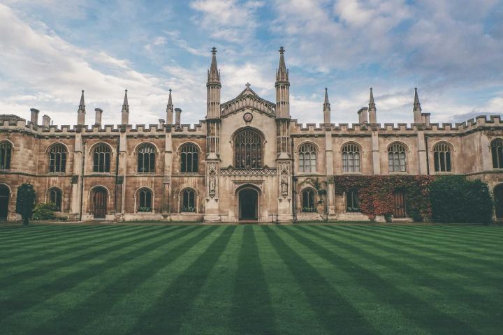 A Gothic stone college building behind a striped lawn
